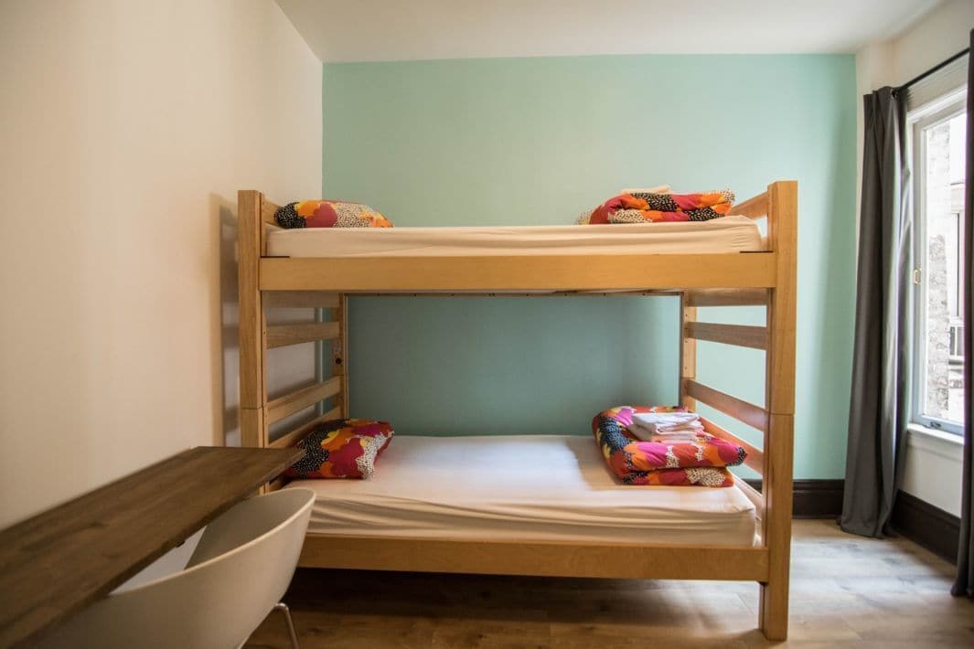 Ein Etagenbett mit bunten Kissen und ein weißer Stuhl in einem Zimmer mit Türkiswänden und einem Fenster mit Vorhängen.
