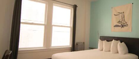 Un dormitorio con cama, ventilador de techo, ventana con cortinas y radiador.