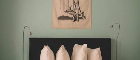 A bed with a dark headboard, a hanging tapestry with a bridge design, and a plain wall.