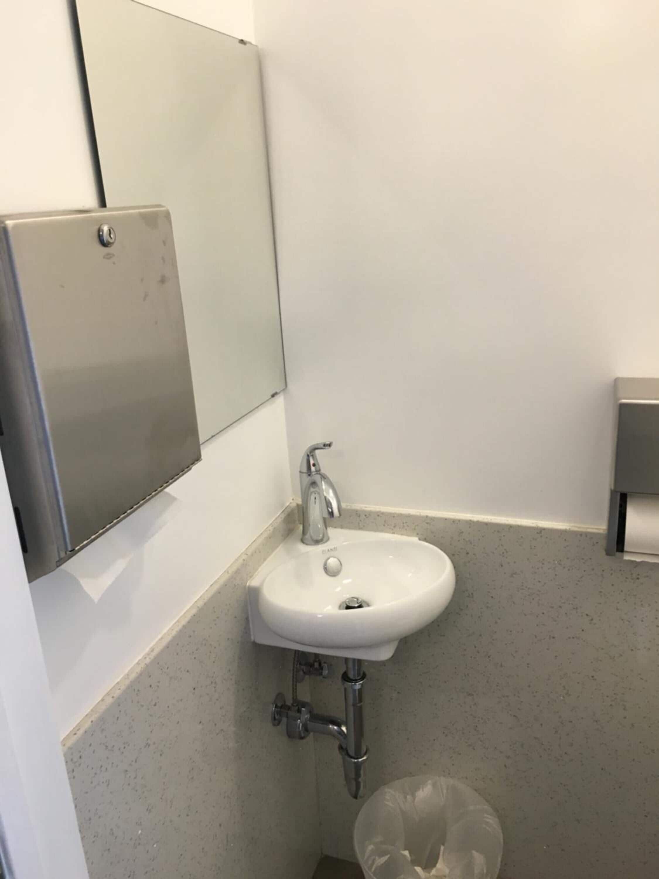 Un baño con un lavamanos blanco, un espejo y un cesto de basura.