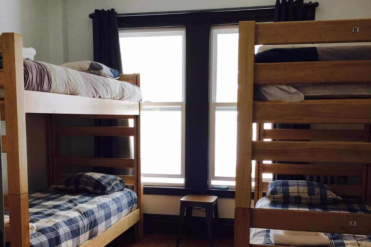 Una camera del dormitorio con due letti a castello, un piccolo sgabello di legno e una finestra con tende.