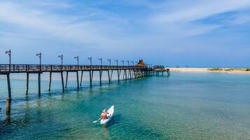 A pier extending into a clear blue sea with a small boat and a person paddling.