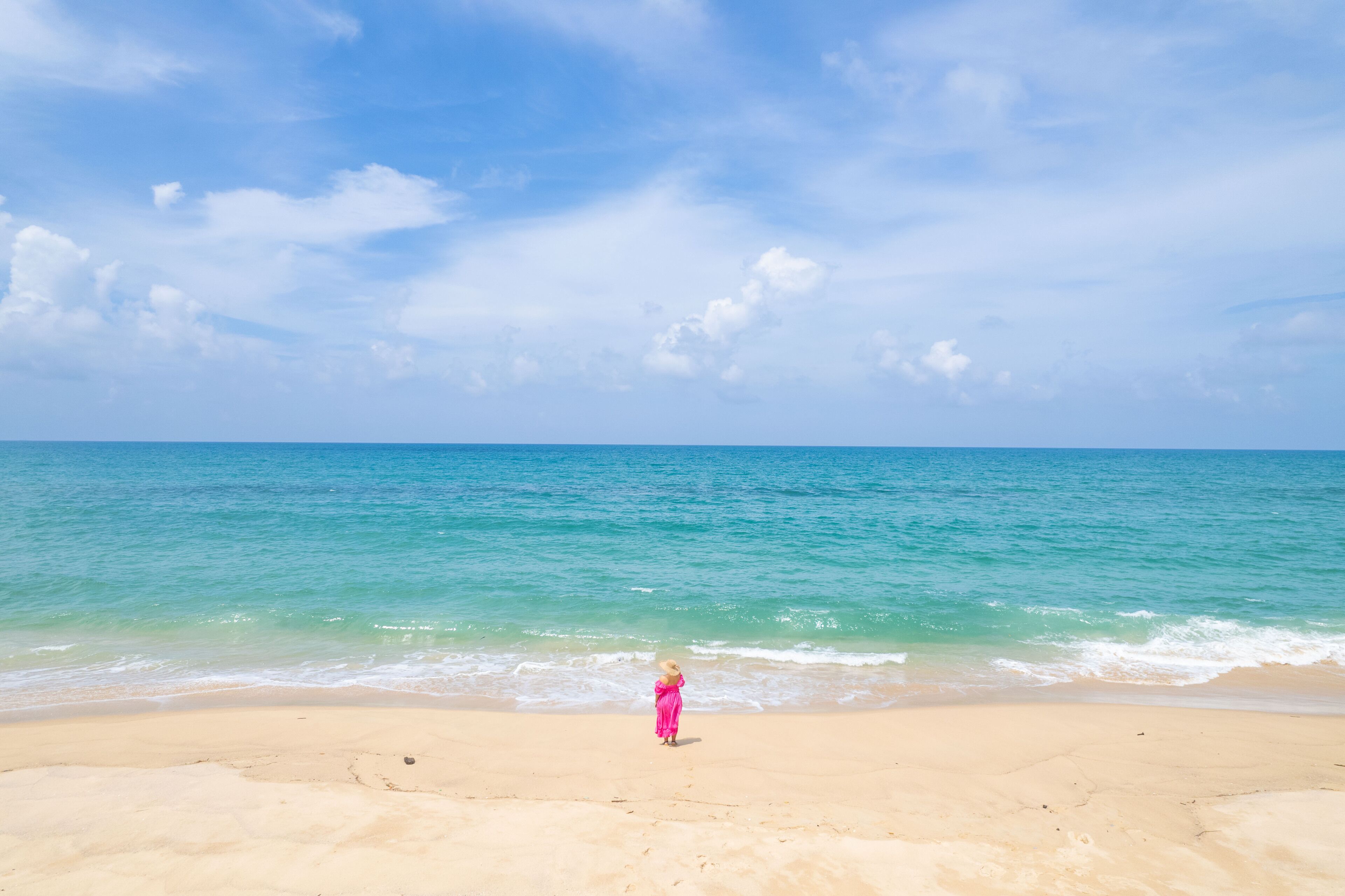 Una playa con agua azul cristalina y un niño vestido de rosa de pie sobre la arena.