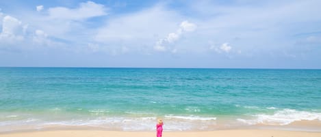 Una playa con agua azul cristalina y un niño vestido de rosa de pie sobre la arena.