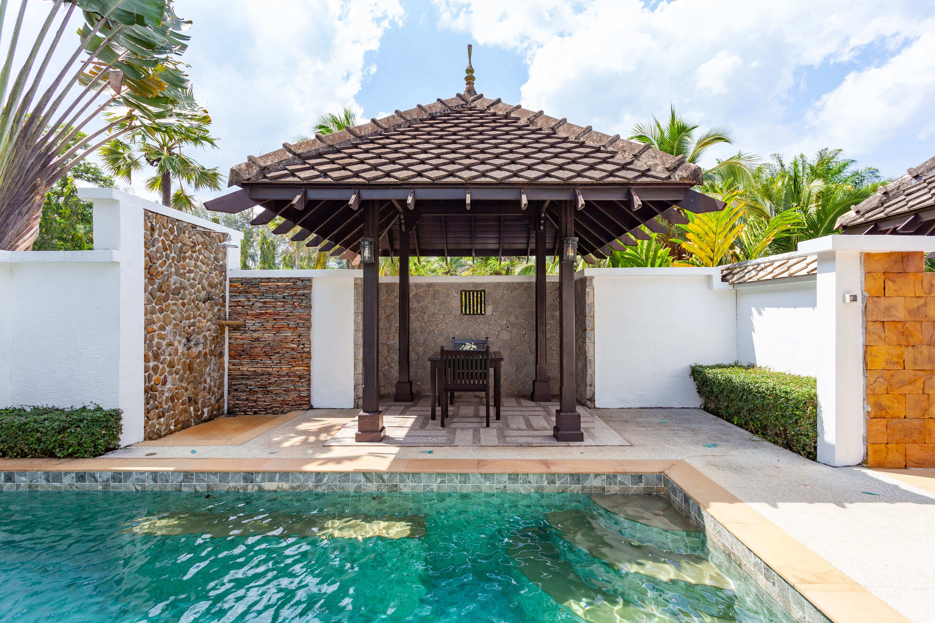 Zona de piscina con pérgola, paredes de piedra y techo de baldosas.