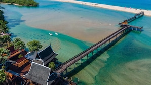 Eine Luftaufnahme einer Küstenlandschaft mit einer hölzernen Pier, die sich ins Meer erstreckt, umgeben von klarem Wasser und einem Sandstrand.