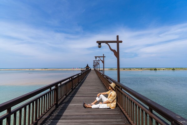 A wooden pier extending over calm water, with a person sitting at the end.