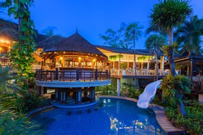 A resort with a pool, a slide, and a bar area.