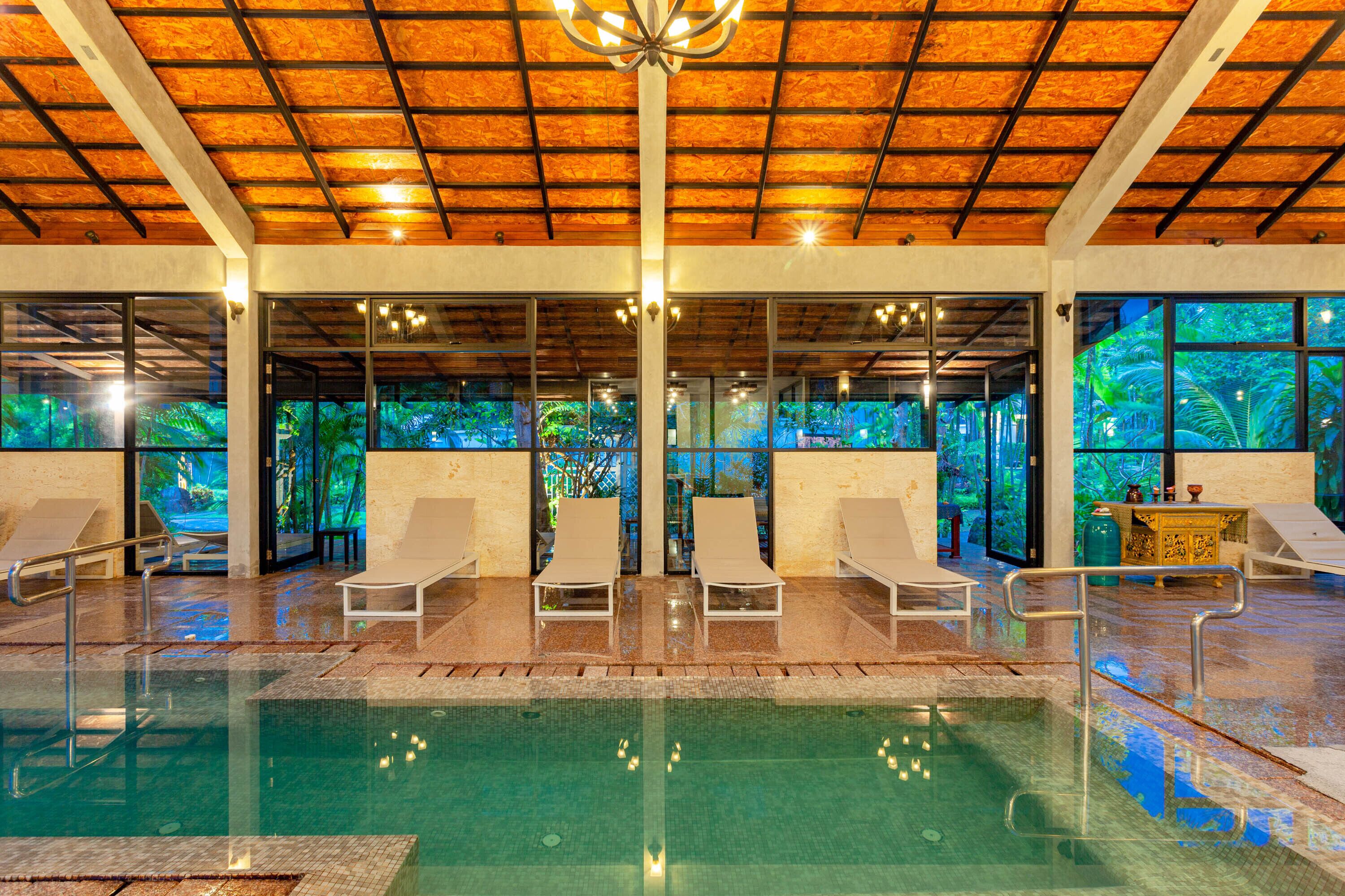 An indoor swimming pool with lounge chairs and a view of greenery through large windows.