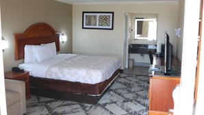 A hotel room with a bed, bedside table, lamp, and a mirror. - Sanger Inn (Sanger)