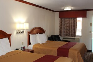 A hotel room with two beds, a desk, a chair, a clock, and a window with patterned curtains.
