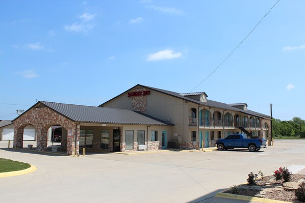 A two-story building with a sign reading "Sanger Inn." It features a brick facade, a flat roof, and a blue pickup truck parked in front. - Sanger Inn (Sanger)