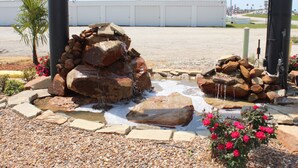 A landscaped area with a rock waterfall, pebbles, and flowers. - Sanger Inn (Sanger)