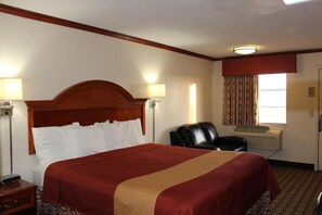 A hotel room with a large bed, a chair, a desk, and a window with curtains.