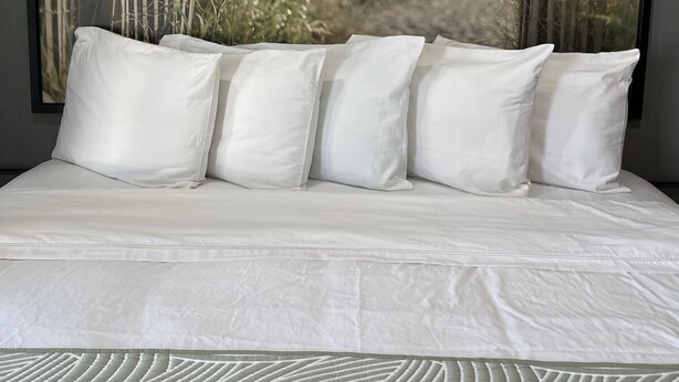 A bed with white bedding and pillows, a large framed beach scene, and a patterned throw at the foot of the bed. -  Valued Stay Mayflower (Madison)