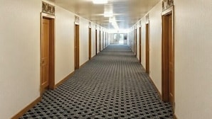 A hotel hallway with wooden doors, numbered 102, and a patterned carpet. -  Valued Stay Mayflower (Madison)