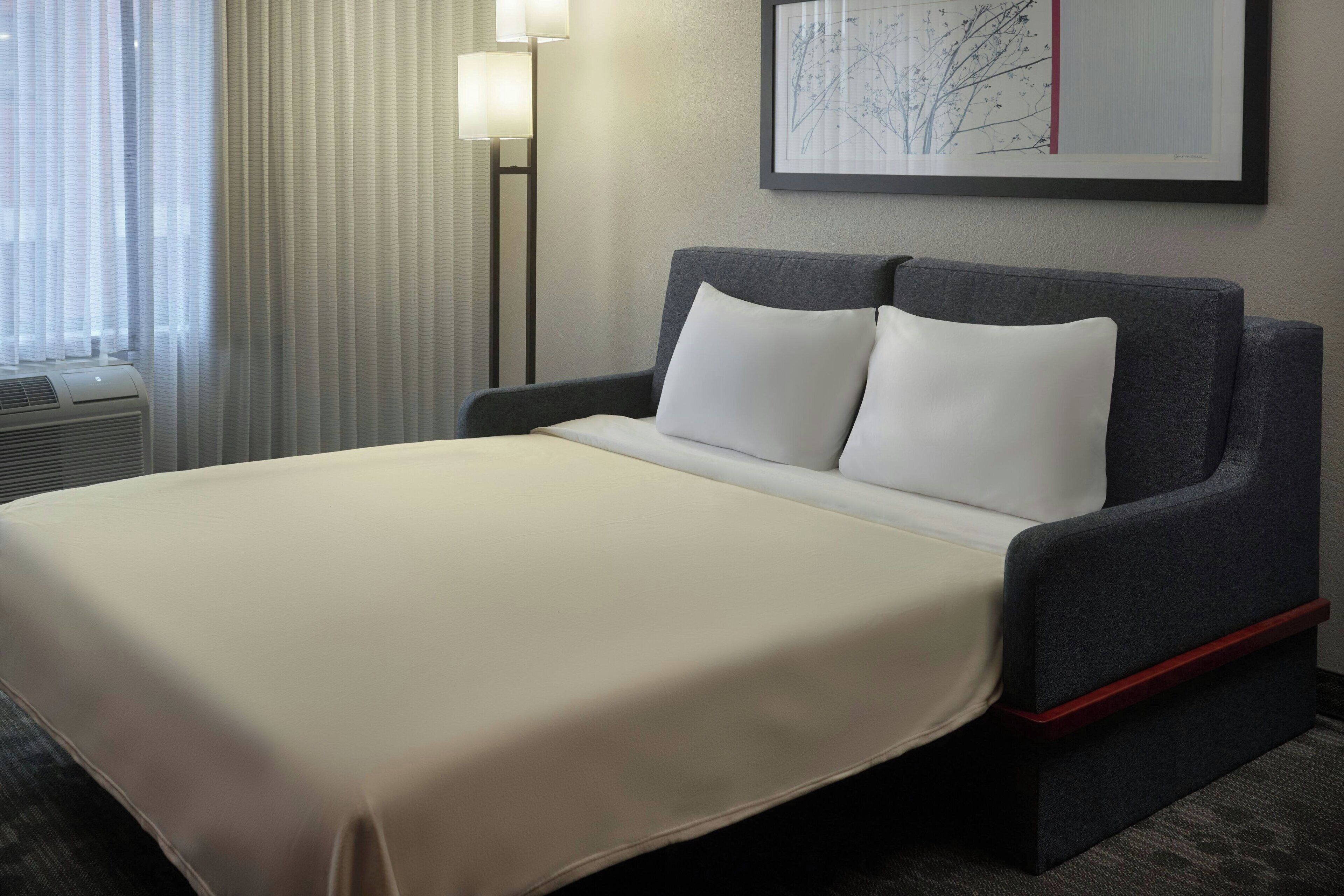 Une chambre d’hôtel avec un lit, une tête de lit, une œuvre d’art accrochée au mur et une lampe sur pied.