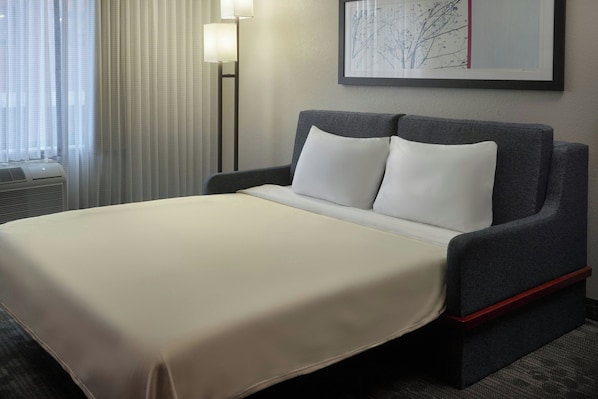 Une chambre d’hôtel avec un lit, une tête de lit, une œuvre d’art accrochée au mur et une lampe sur pied.