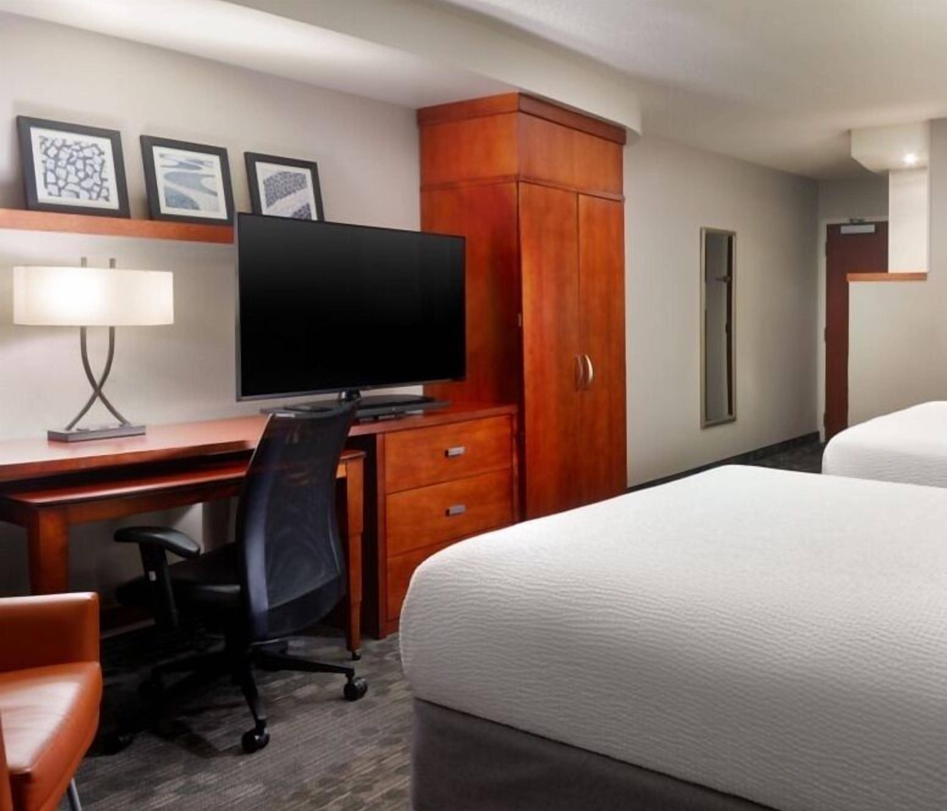 Una habitación de hotel con una cama, un escritorio con computadora y una silla, un televisor y un armario.