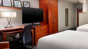 Una habitación de hotel con una cama, un escritorio con computadora y una silla, un televisor y un armario.