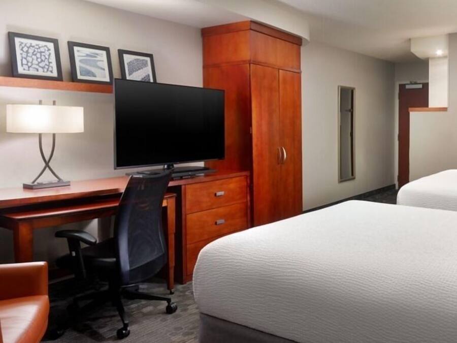 Una habitación de hotel con una cama, un escritorio con computadora y una silla, un televisor y un armario.