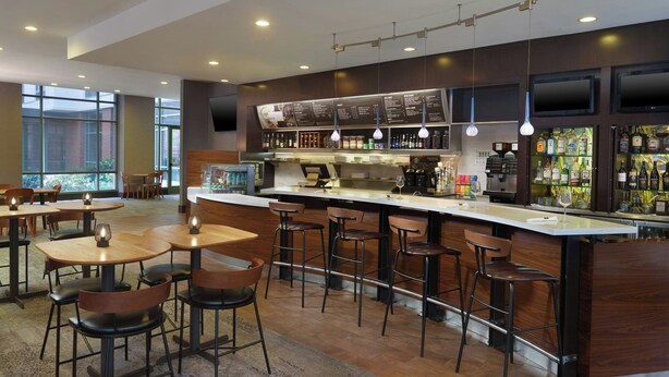 Zona de bar moderna con una barra larga, varios taburetes y una pantalla de menú.