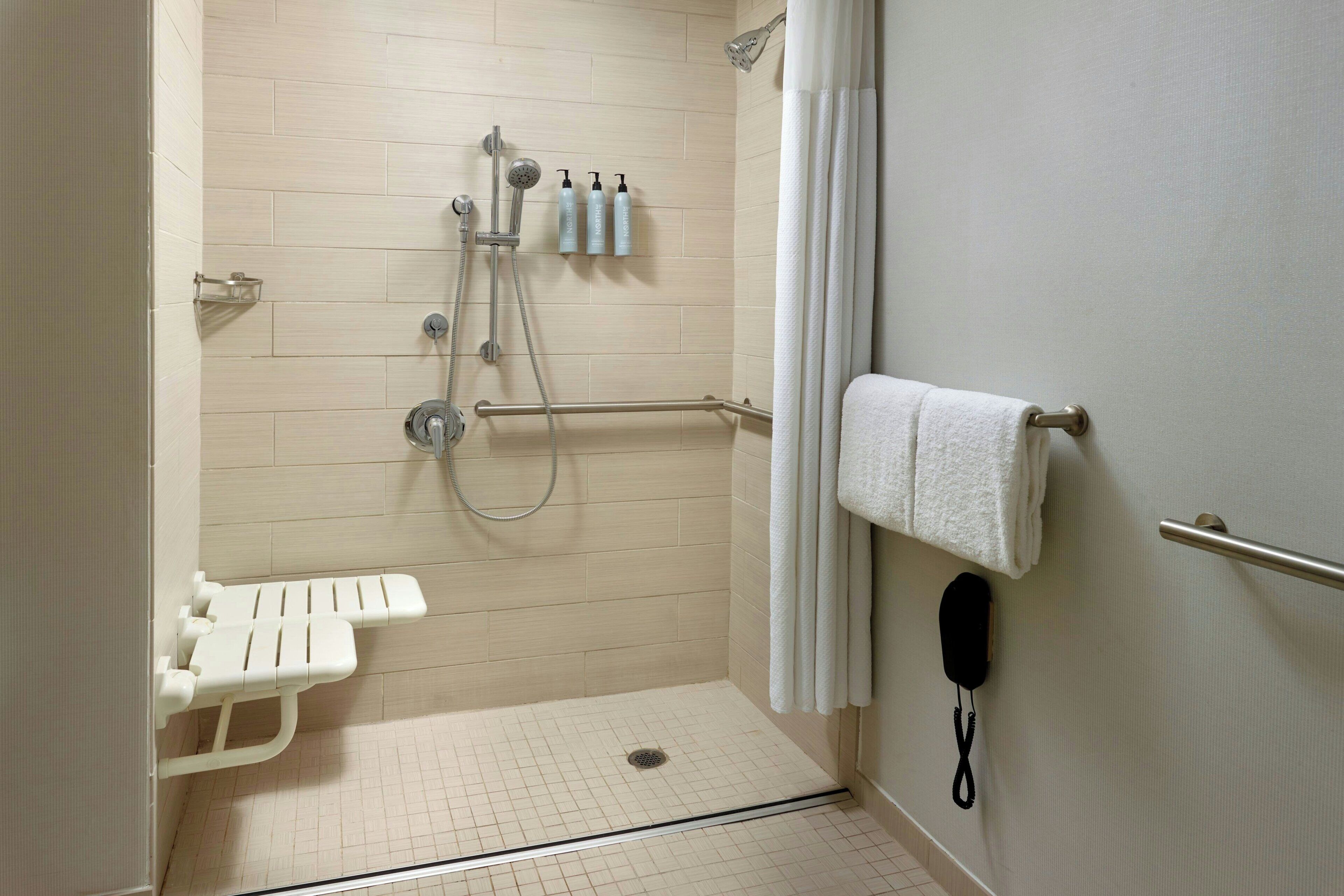 Zona de ducha accesible para sillas de ruedas con asiento, barras de apoyo y ducha de mano.
