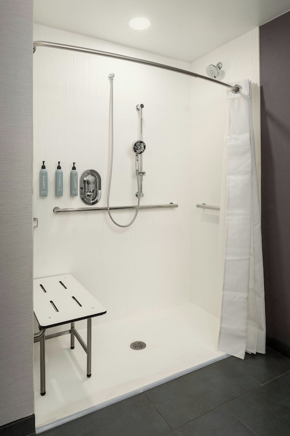 Un espace douche moderne avec une paroi en verre, une douchette à main et une petite table sur laquelle sont posés des articles de toilette.