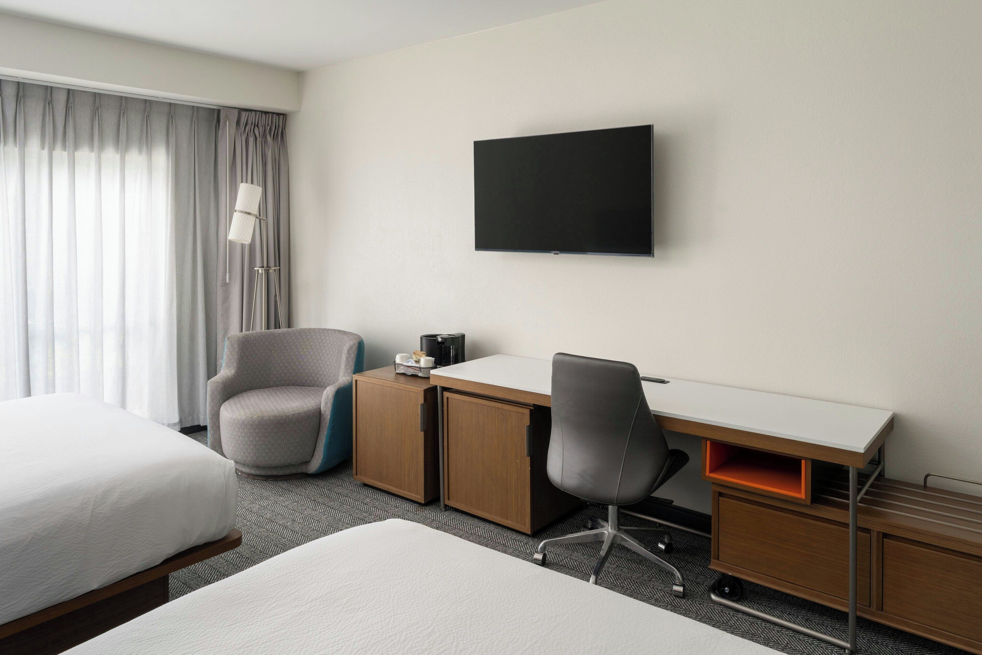 Una habitación de hotel con dos camas, un escritorio, una silla, un televisor y una lámpara.