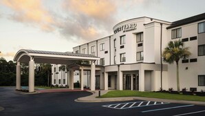 A Courtyard by Marriott hotel with a covered entrance, multiple floors, and a palm tree. - Courtyard by Marriott Brunswick (Brunswick)