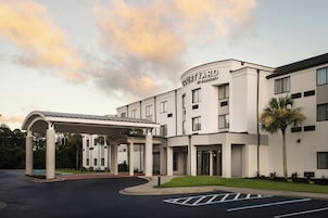 Un hotel Courtyard by Marriott con entrada cubierta, varios pisos y una palmera.