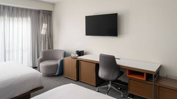 A hotel room with a bed, a desk with a chair, a flat-screen TV, and a lamp.