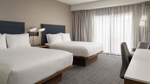 A hotel room with two beds, a desk, a chair, and a large window with curtains. - Courtyard by Marriott Brunswick (Brunswick)