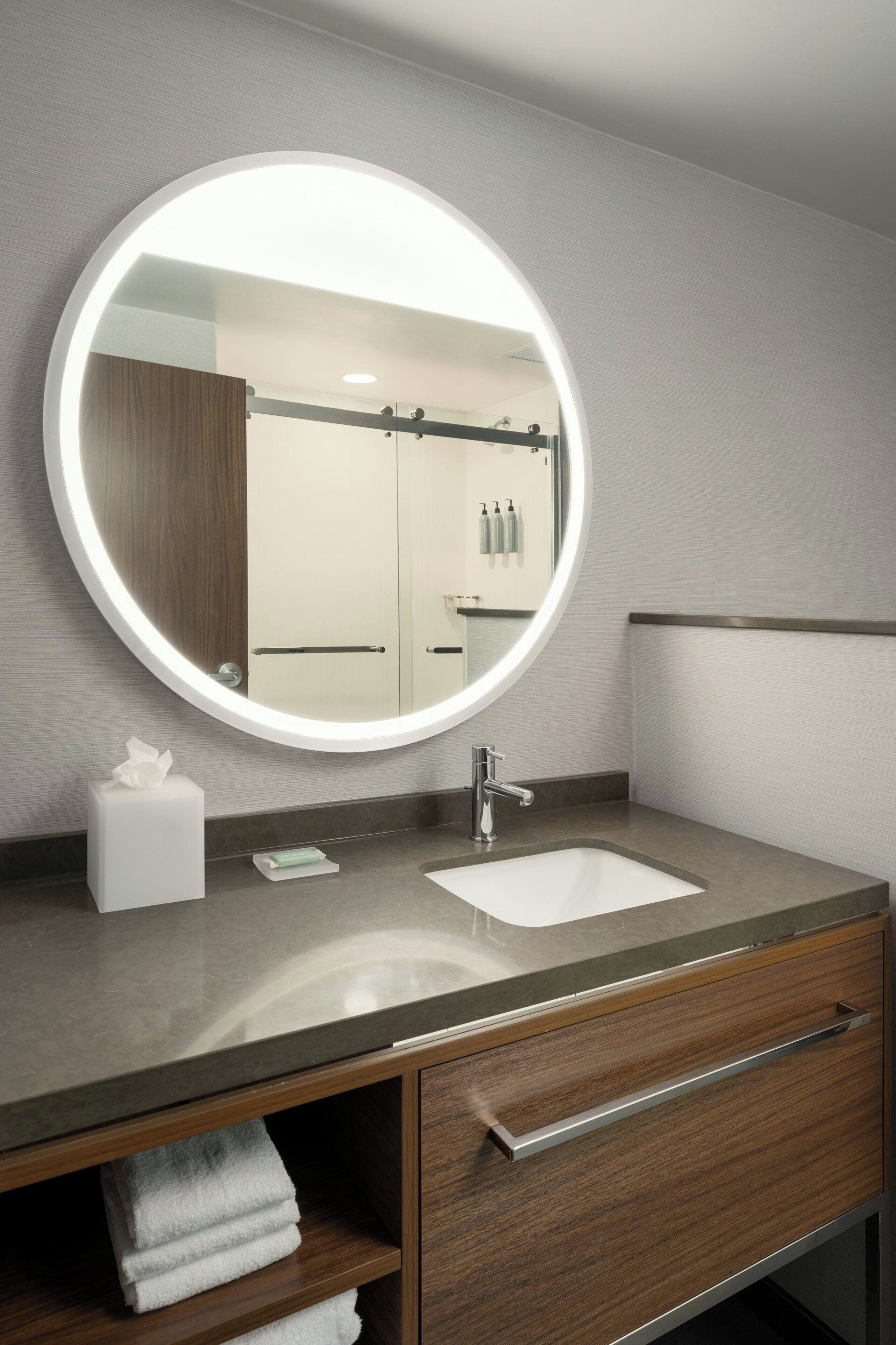 Un baño moderno con un espejo redondo, un lavabo y un perchero para toallas.