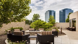 Un patio exterior con mobiliario de mimbre, una chimenea y vistas a dos rascacielos.