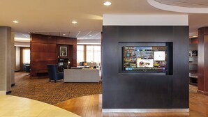 Un vestíbulo con mostrador de recepción, zona de estar y un panel informativo digital.
