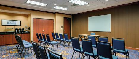 A conference room with a carpeted floor, rows of chairs, a projector screen, and a presentation area.