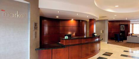A reception area with a curved wooden reception desk, a sign reading "market", and a check-in counter.