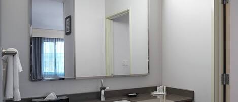 A modern bathroom with a large mirror, a sink, a towel rack, and a tissue box.
