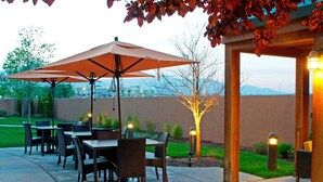 Un patio al aire libre con mesas y sillas, una pérgola con luces y vistas a la ciudad al fondo.