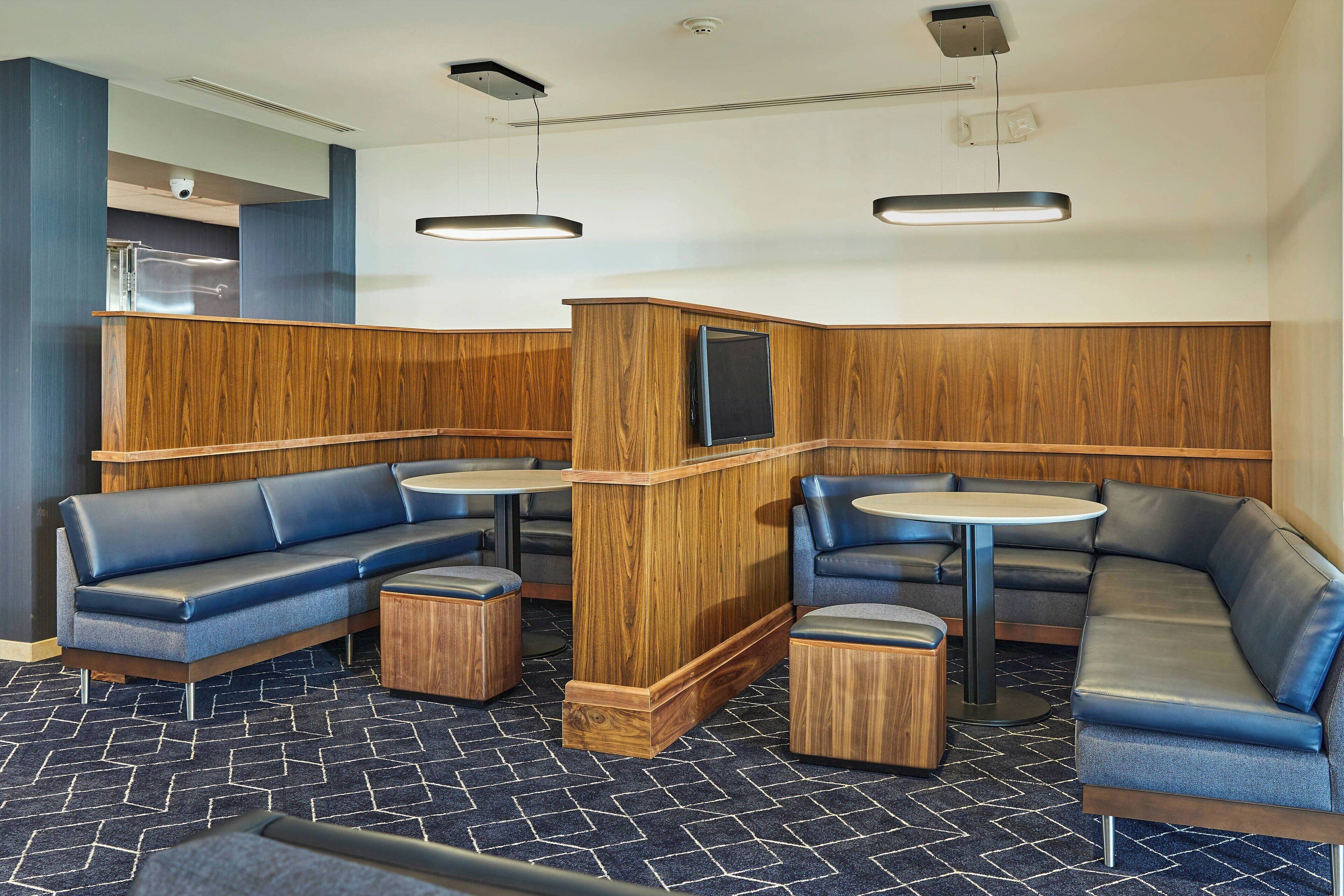 A modern lounge area with wooden paneling, blue leather seating, and round tables.