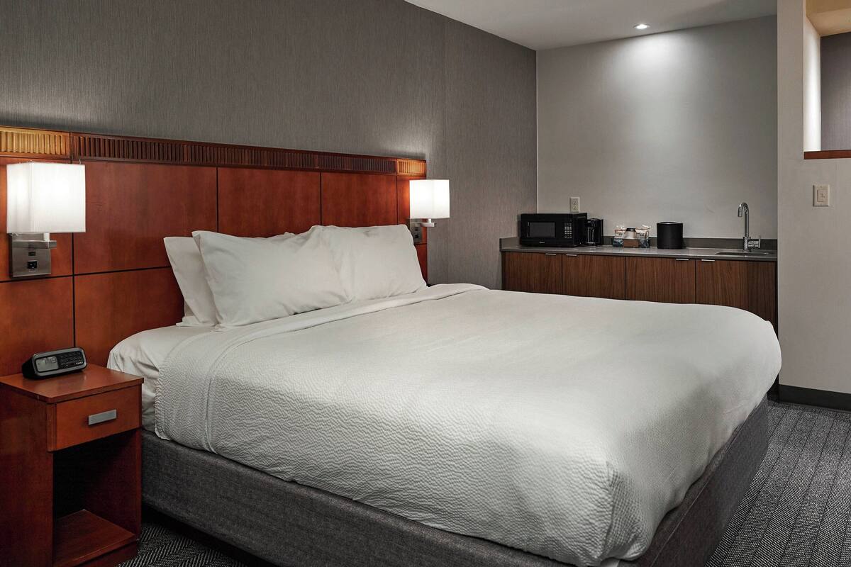 Een hotelkamer met een groot bed, nachtlampjes, een nachtkastje, een magnetron en een kleine kitchenette.