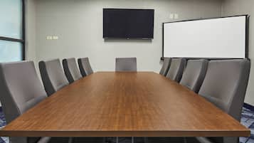 Una sala de conferencias con una larga mesa de madera, sillas tapizadas en gris, un televisor de pantalla plana grande y una pizarra.