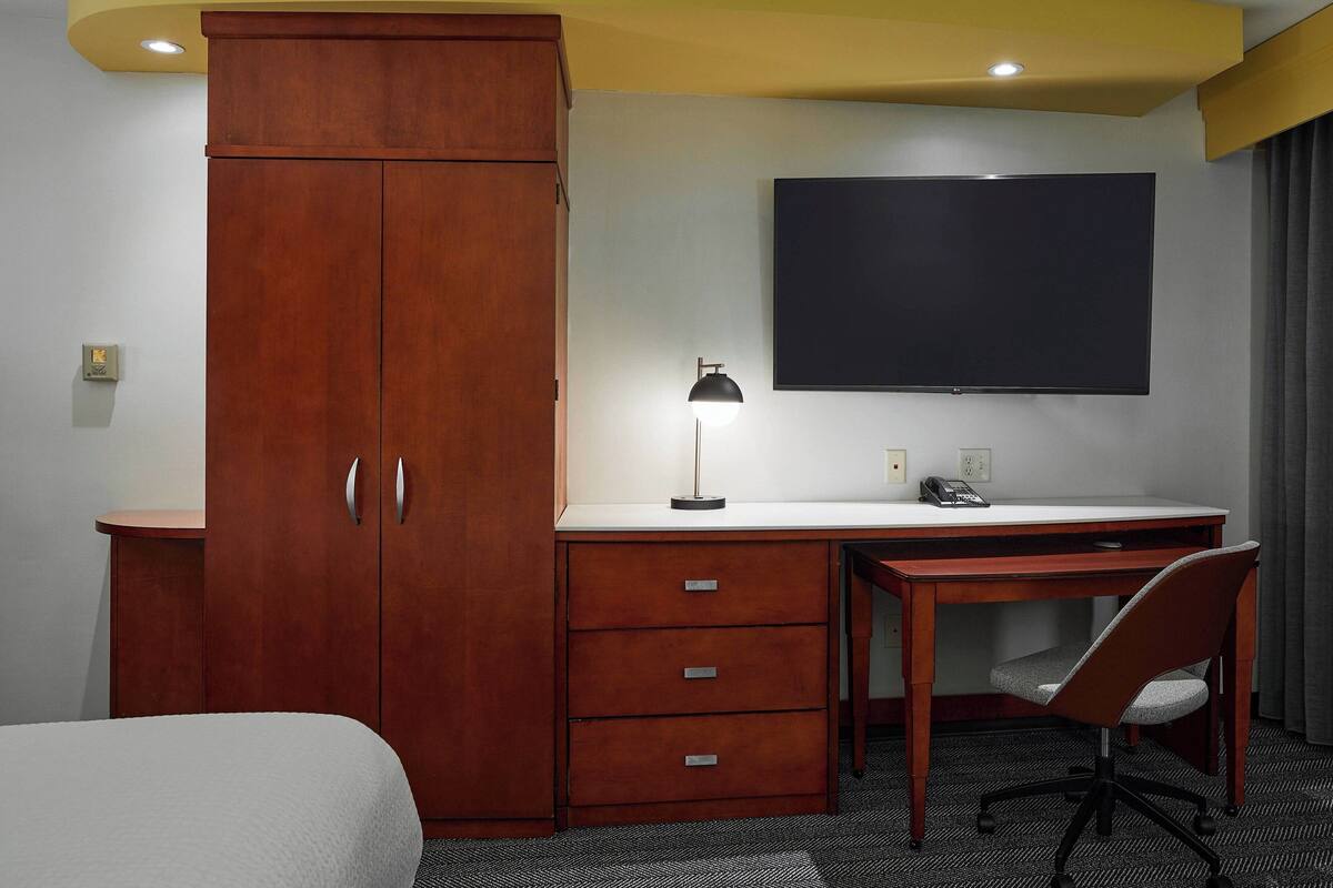 Een hotelkamer met een houten garderobe, een bureau met stoel, een flatscreen televisie en een bureaulamp.