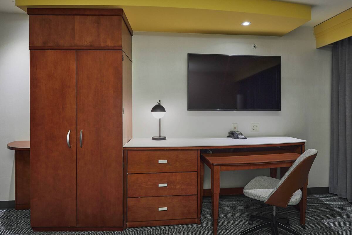 Een hotelkamer met een houten garderobe, een bureau met stoel, een flatscreen televisie en een bureaulamp.