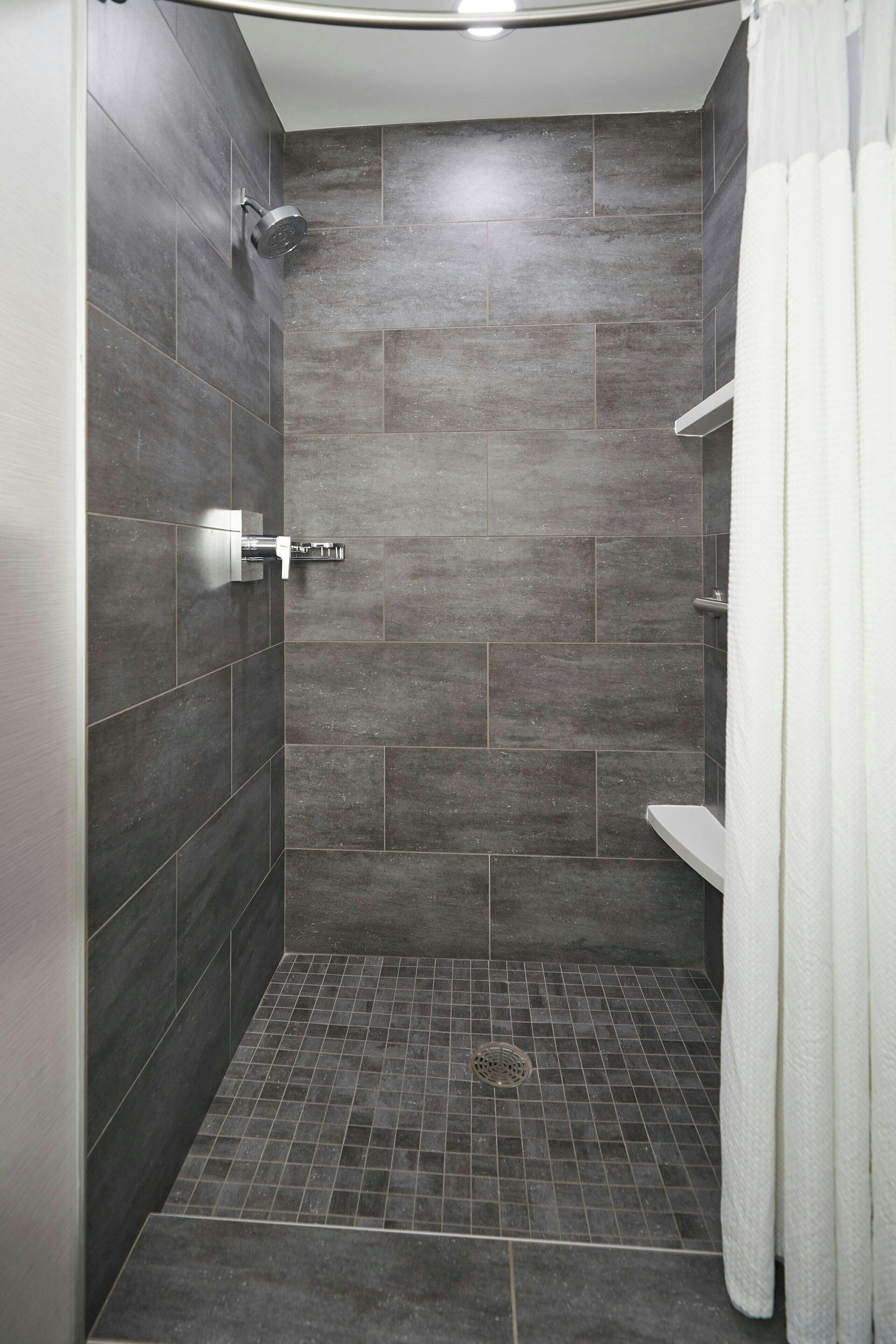 A modern shower area with dark tiles, a showerhead, and a white towel hanging on a rack.