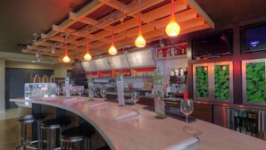 Una zona de bar con un mostrador curvo, taburetes, lámparas colgantes, una pizarra de menú y una pantalla de televisión.