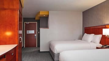 Une chambre d’hôtel avec deux lits, une armoire en bois, un bureau et une petite table de chevet avec une lampe.