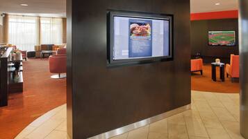 A modern hotel lobby with a large digital screen displaying a menu, comfortable seating areas, and a sports-themed wall decoration.