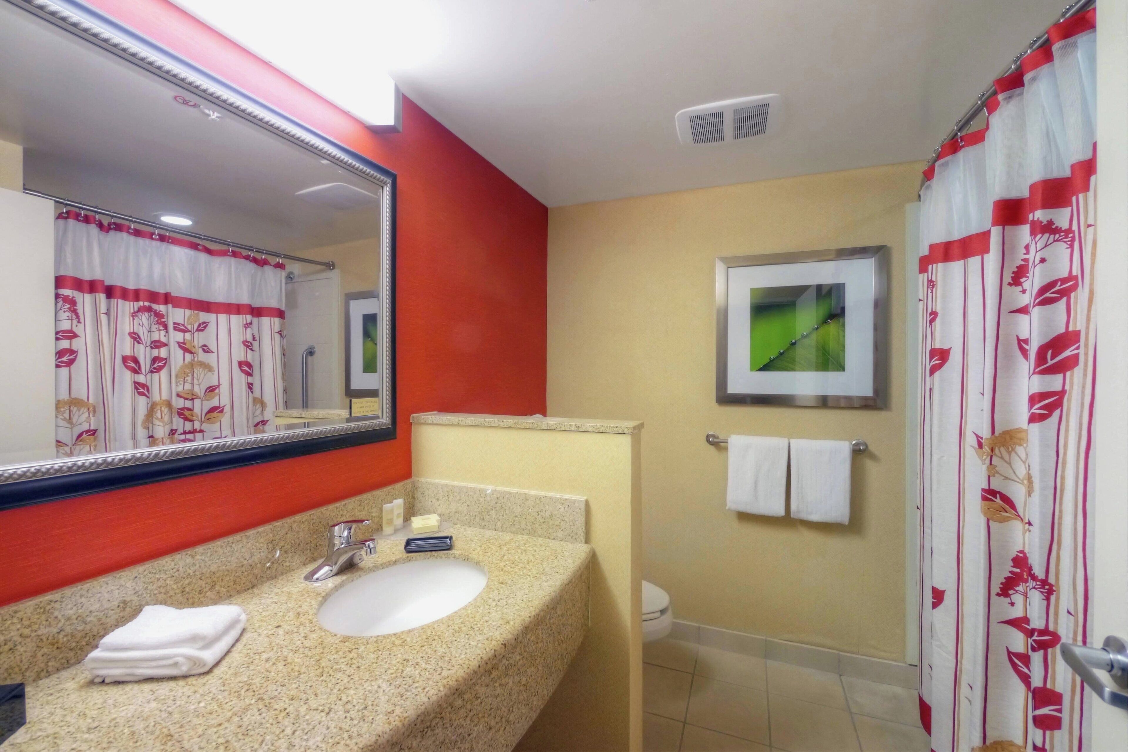 A bathroom with a granite countertop sink, a mirror, a toilet, and a shower curtain with a floral pattern.